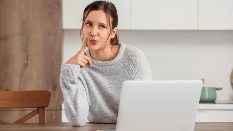 Eine Frau sitzt am Laptop und sieht aus, als würde sie gerade eine Idee haben