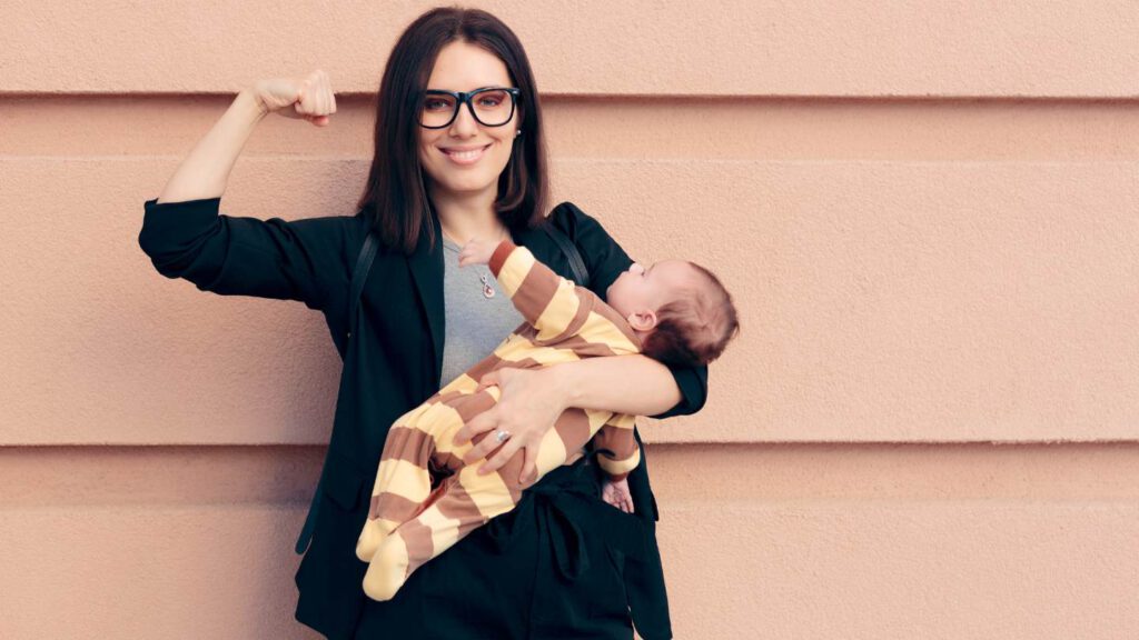 Eine Frau im schwarzen Blazer hält im einen Arm ein Baby, den anderen Arm spannt sie an als Symbol der Stärke.